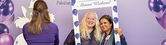 Alumni Weekend: 2 Women Posing with an Alumni Weekend Foam Core Frame having their picture taken