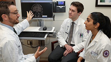 An instructor points to a computer screen of a brain scan to train two students.