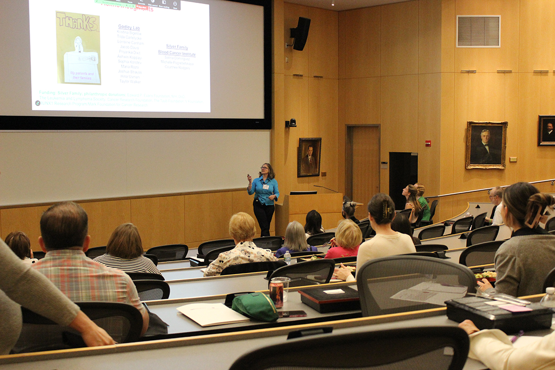 Patients, donors, and friends seated in an auditorium listen to Lucy Godley lecture
