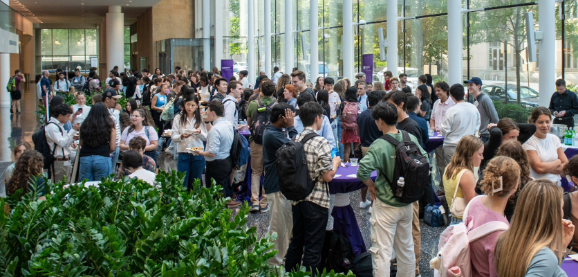 Attendees gather in small groups, talking and enjoying refreshments at tables during the event