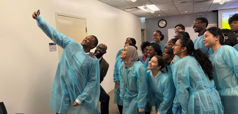 A group of students and faculty in blue scrubs taking a group photo