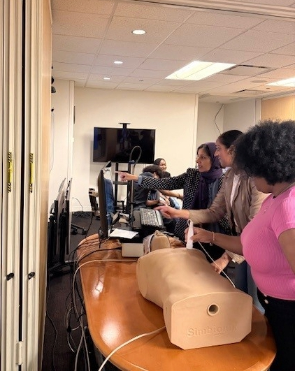 A student using a heart tool on a medical mannequin as two women assist