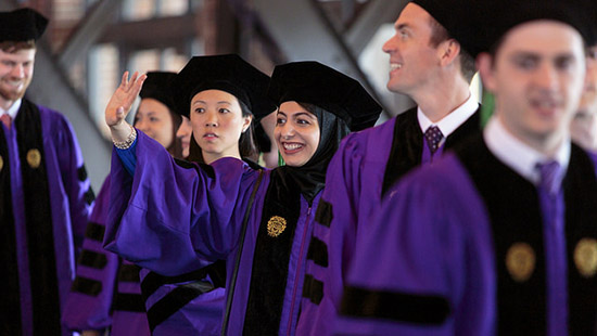 Graduating MD students, smiling and waiving in their robes and caps
