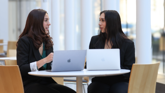 Two students talk and look at laptops