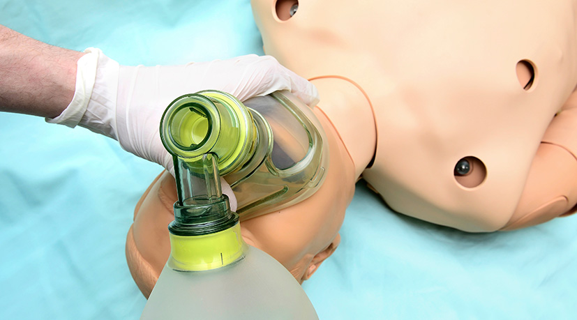 A student practices the placement of a respiratory apparatus on a practice dummy