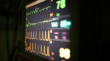 A glowing monitor displays vitals in a dark room