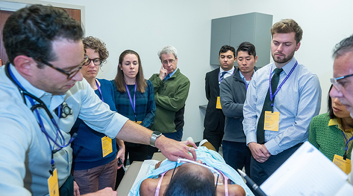 A group of medical faculty and residents at Northwestern Feinberg School of Medicine participating in a Bedside Excellence Development Series (BEDS) session, gathered around a patient bed for a clinical teaching demonstration.