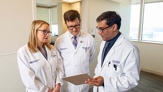 Three physicians in white coats huddle around a clipboard.