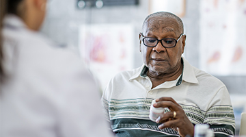 An older gentleman is looking at a pill bottle.