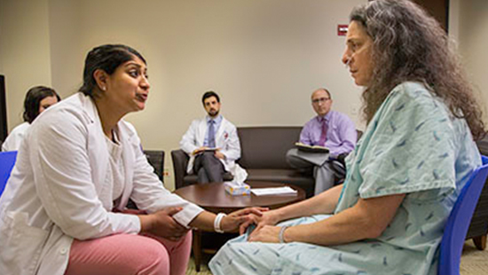 An instructor practices communication skills, touching a patient's hand.
