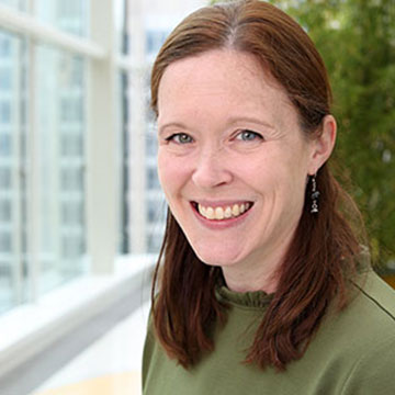 Mary McBride smiles near a window with greenery behind her.