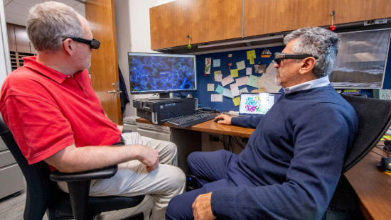 Two research faculty wearing VR-like glasses discussing computer image