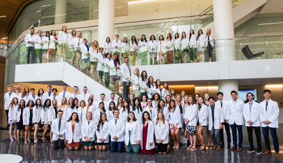 A group of physical therapists in white coats line up from the bottom to the top of a staircase