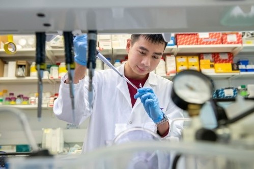 lab worker seen through shelves holding a pipette and test tube